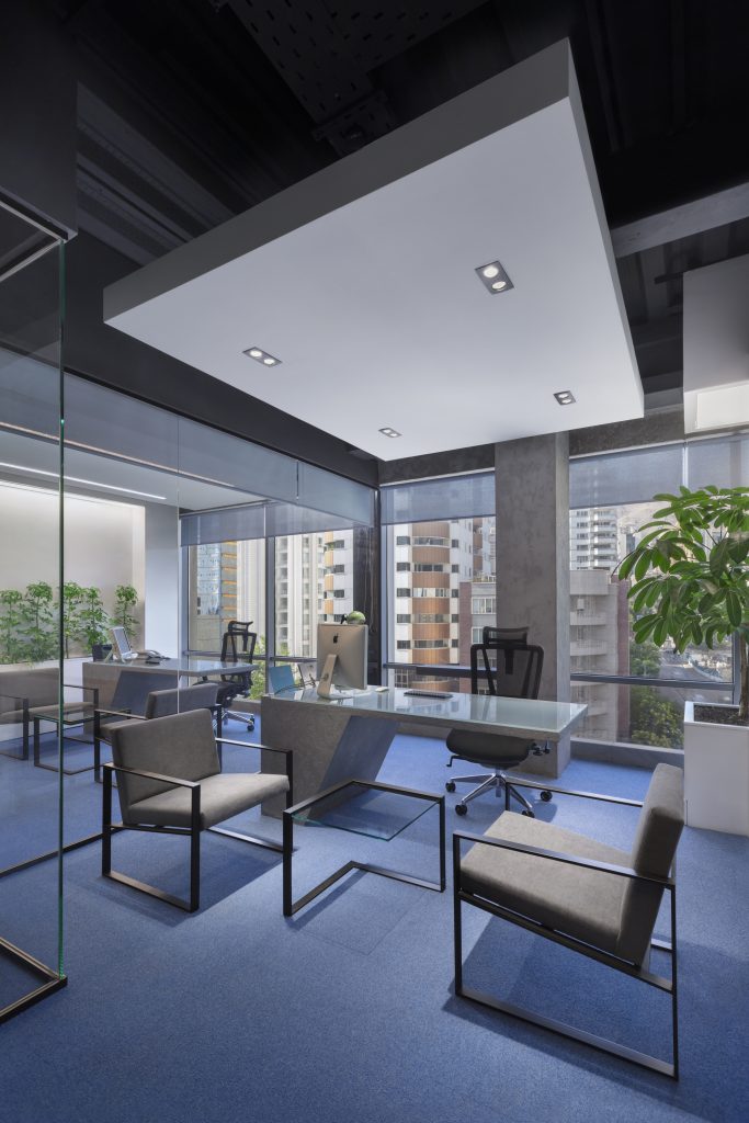 Manager’s office with a glass desk, gray armchairs and blue carpet.