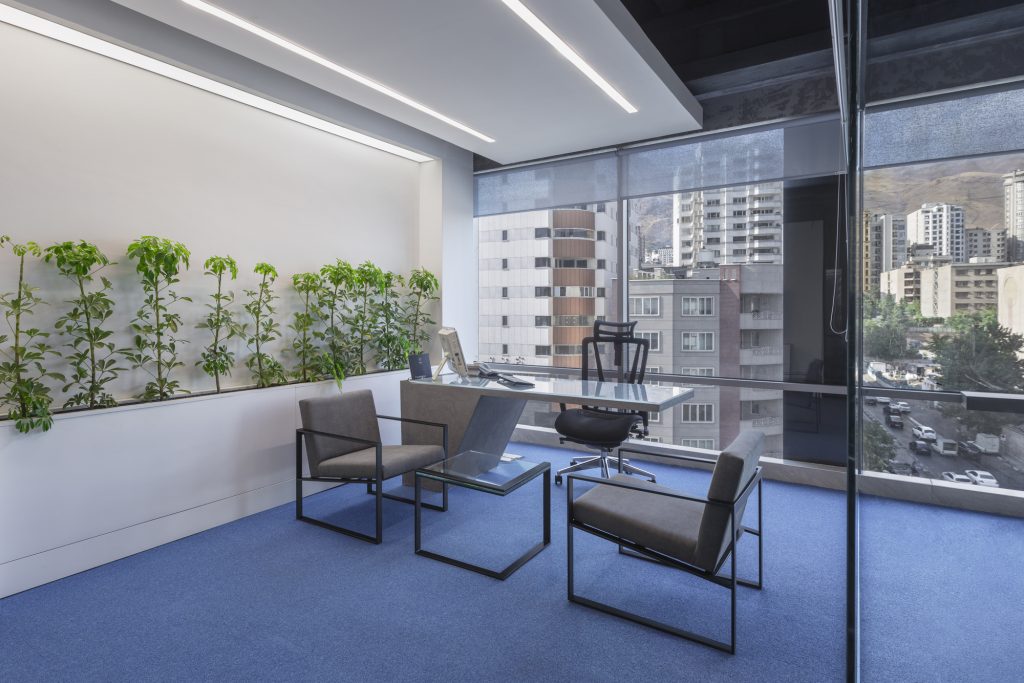 Office with a planter wall, a glass desk and a window over the city.