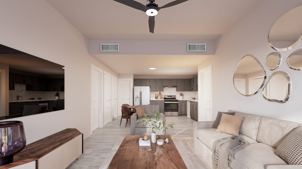 The model unit’s living room with a cream sofa, a wood coffee table, round mirrors and a TV, opening to a kitchen with stainless appliances.