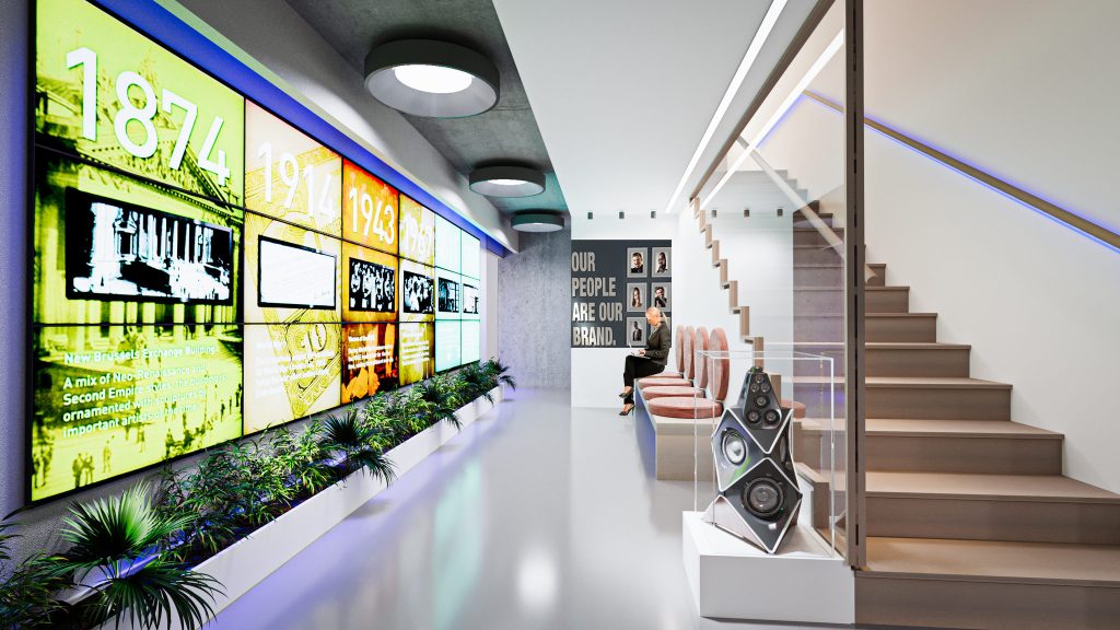 A corridor with a long lit timeline wall above a planter, a speaker on display and a wood stair to the upper floor.