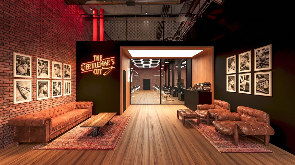 A lounge with brown leather chesterfield sofas, framed black-and-white prints on red brick and a neon sign, with glass doors to the barber area.