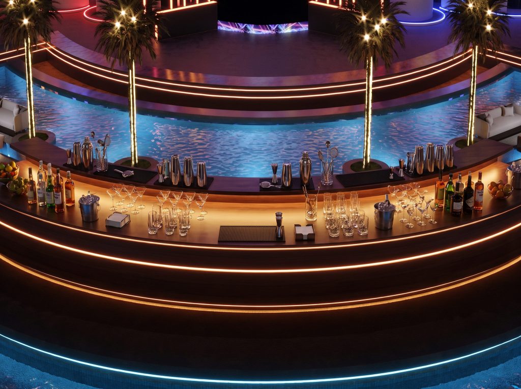 A curved bar counter lit in warm orange in the foreground, with the reflecting pool, palm trees and the stage beyond.
