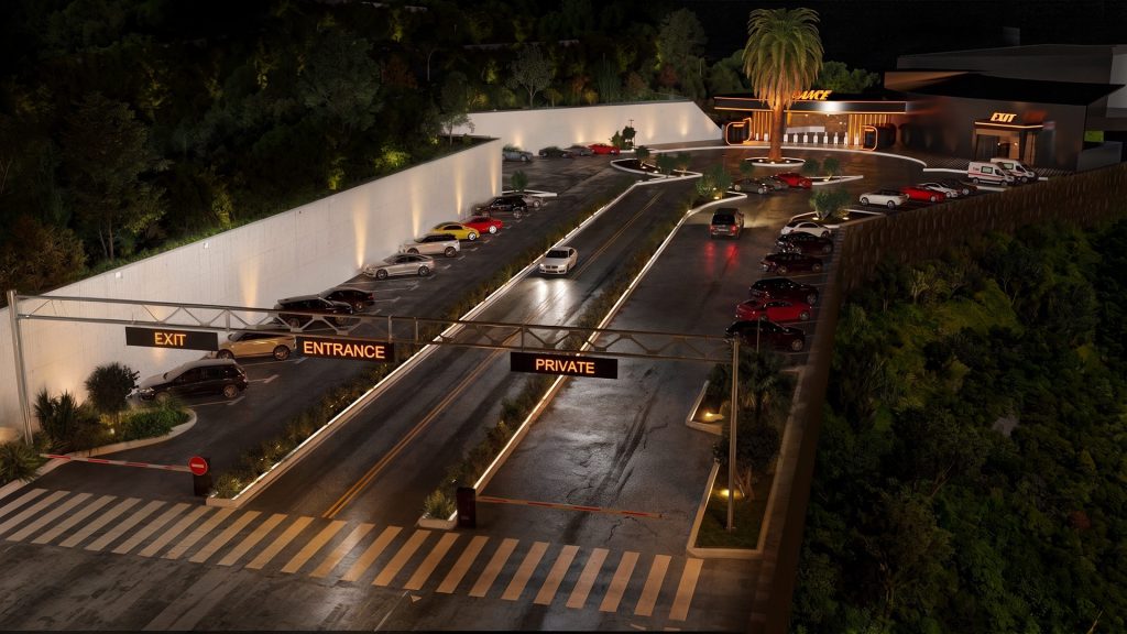 An aerial night view of the nightclub drive, with exit, entrance and private lane signs on a gantry, a lit retaining wall and parked cars up to the entrance.
