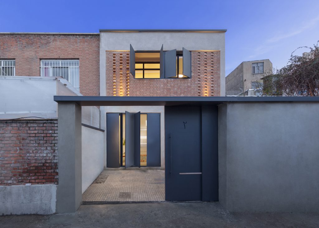 The same street front at dusk, with the shutters open and warm light inside.