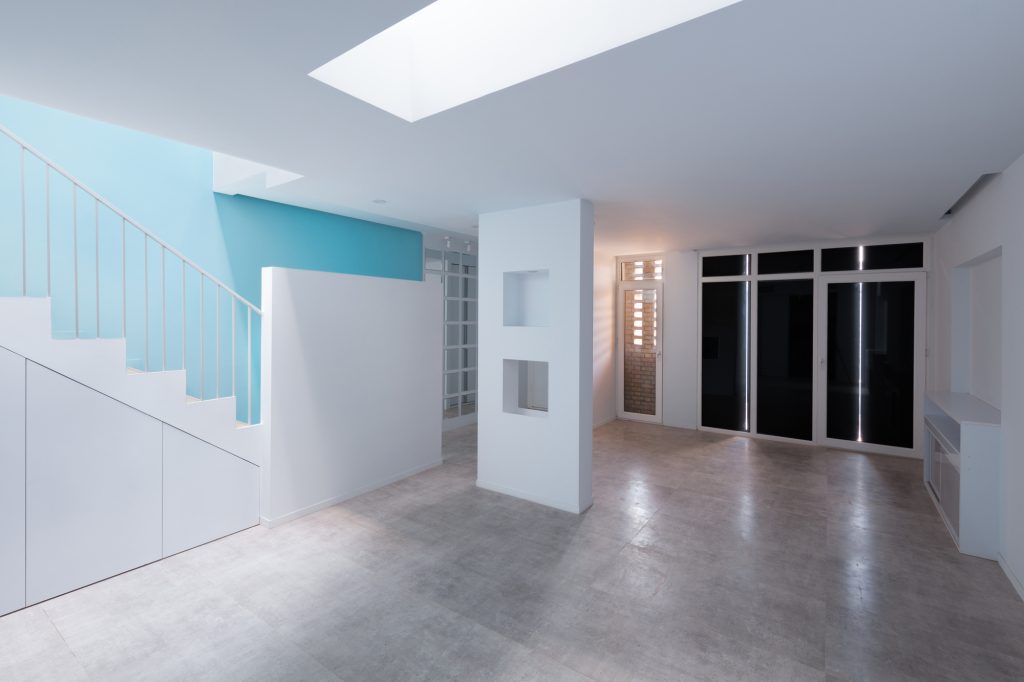 Ground floor with the sky-blue stair, a white partition with small openings and dark glass doors.