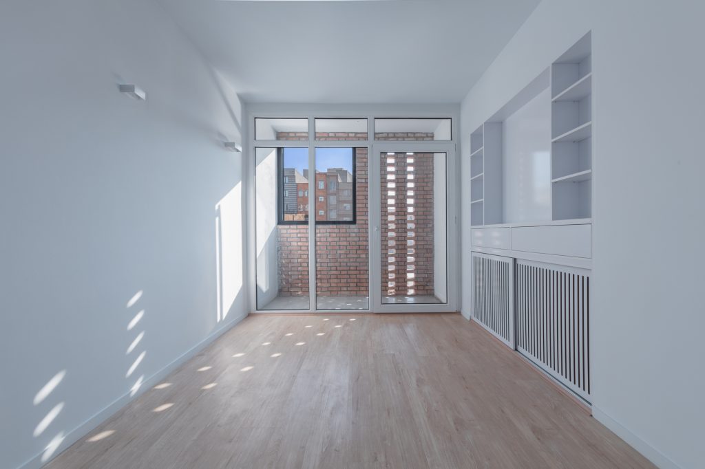 Upstairs room with a wood floor, daylight through the brick screen and built-in white shelving.