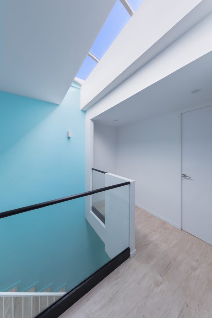 Stair landing with a sky-blue wall, a glass balustrade and a skylight above.
