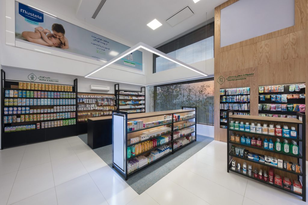 A pharmacy corner with black shelving of care products, a wood-clad wall and a large lit photo panel above the displays.