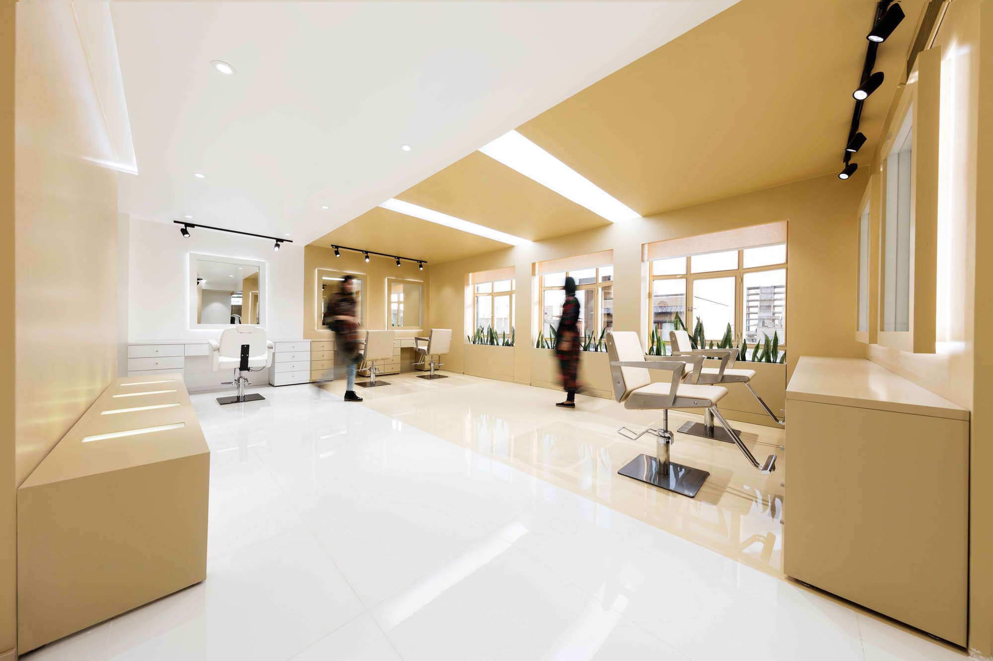 Shokrniya Beauty Salon: golden ochre walls and ceiling over white glossy floors, with styling chairs and light slots overhead.