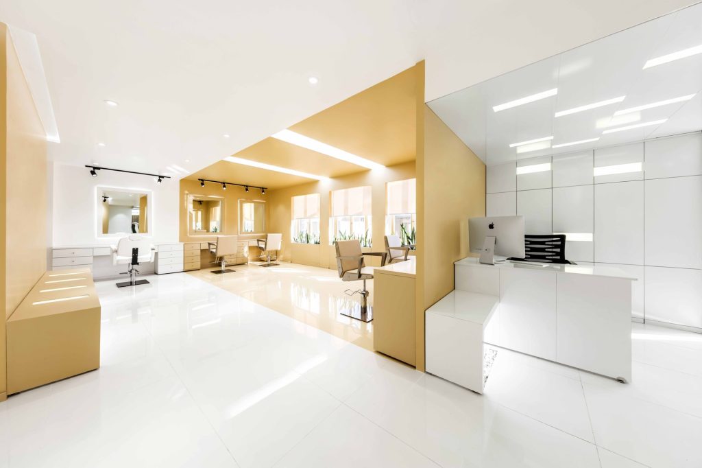 Reception desk in a white glass box beside the golden salon floor.