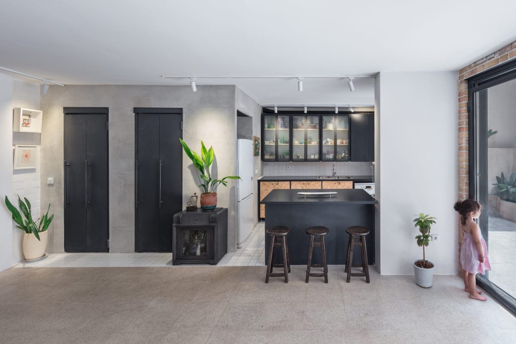 A kitchen with black cabinets and glass-front uppers, a black island with wood stools and a child by the glass door.