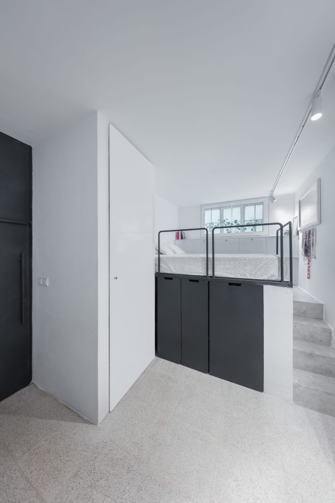 A narrow white space with a raised bed area above black storage, reached by small steps.
