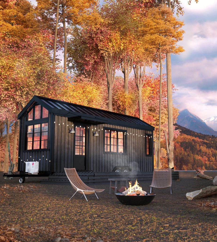 A black modern tiny cabin with string lights among autumn trees, with a lounge chair and a fire pit in front.