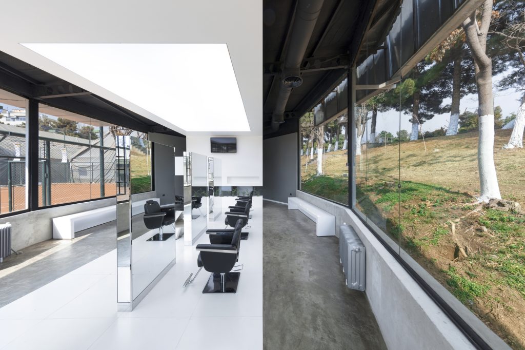 Salon chairs facing slim mirrors, with a glass wall onto the trees.