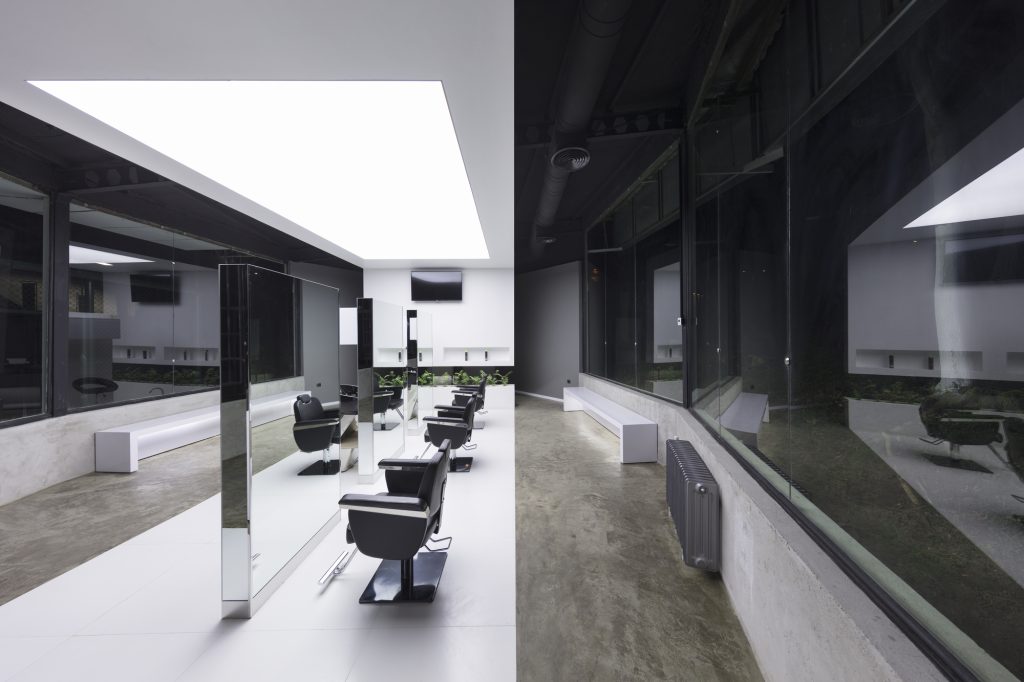 A row of black salon chairs and mirrors under the white ceiling panel.