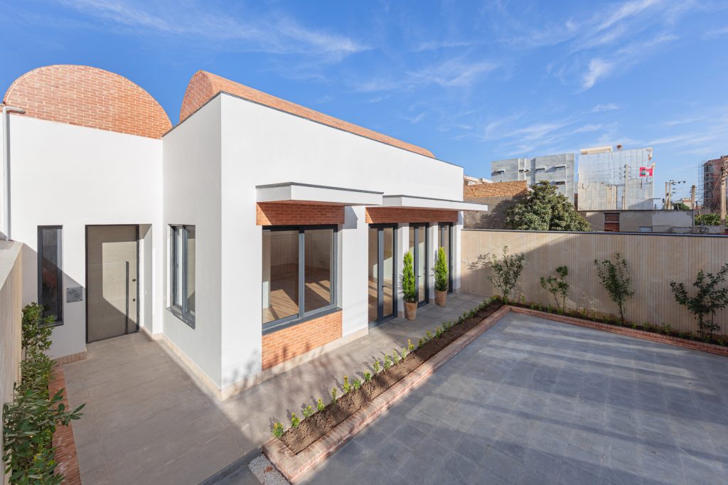 The courtyard by day: white walls, brick window hoods, gray paving and a long planter.