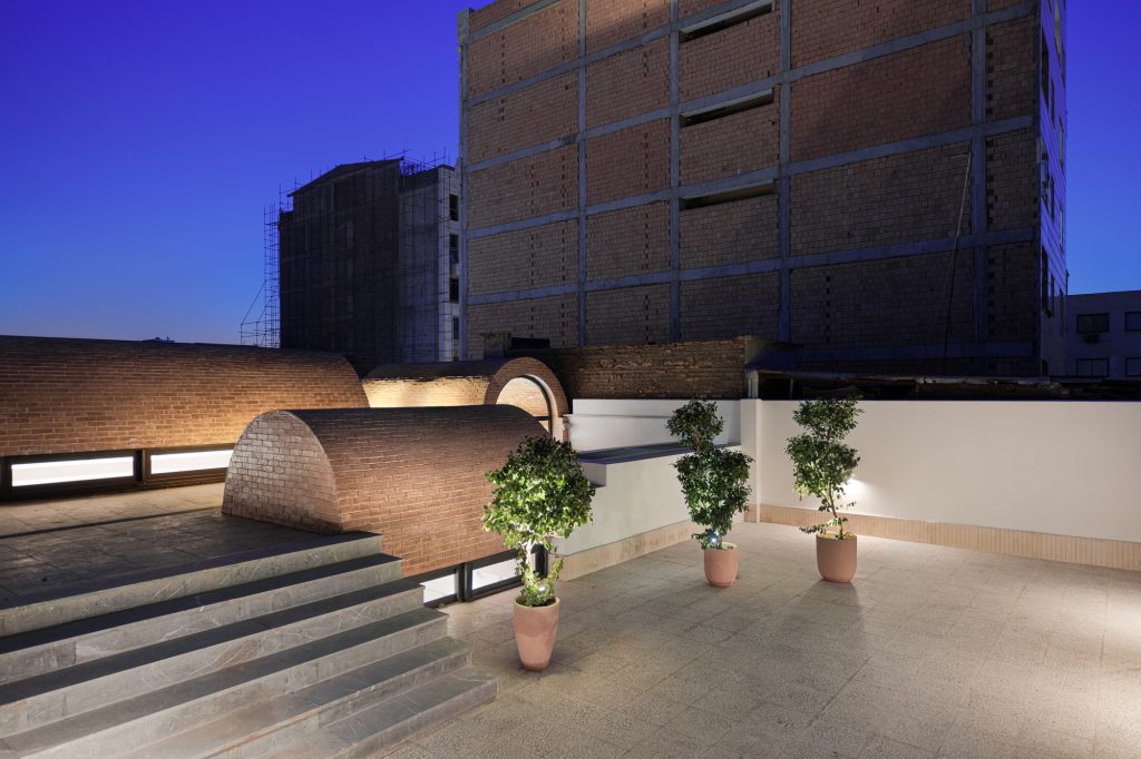 Roof terrace at dusk with brick barrel vaults, wide steps and potted trees.