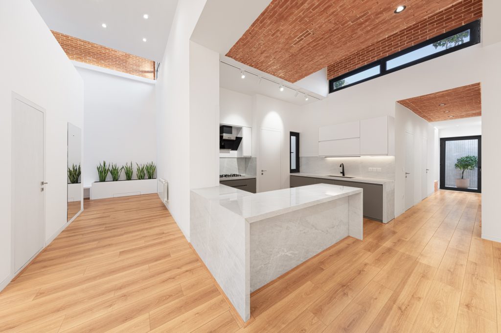 Kitchen with a white stone island under an exposed brick vault and a high clerestory window.
