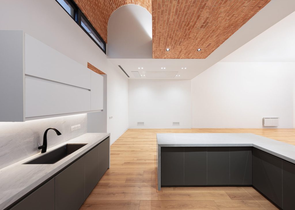 Kitchen with dark lower cabinets, white upper cabinets and a brick vault overhead.