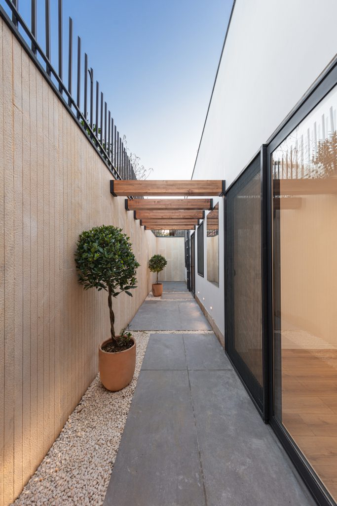 Narrow side courtyard with a stone path, a potted tree and a timber pergola.